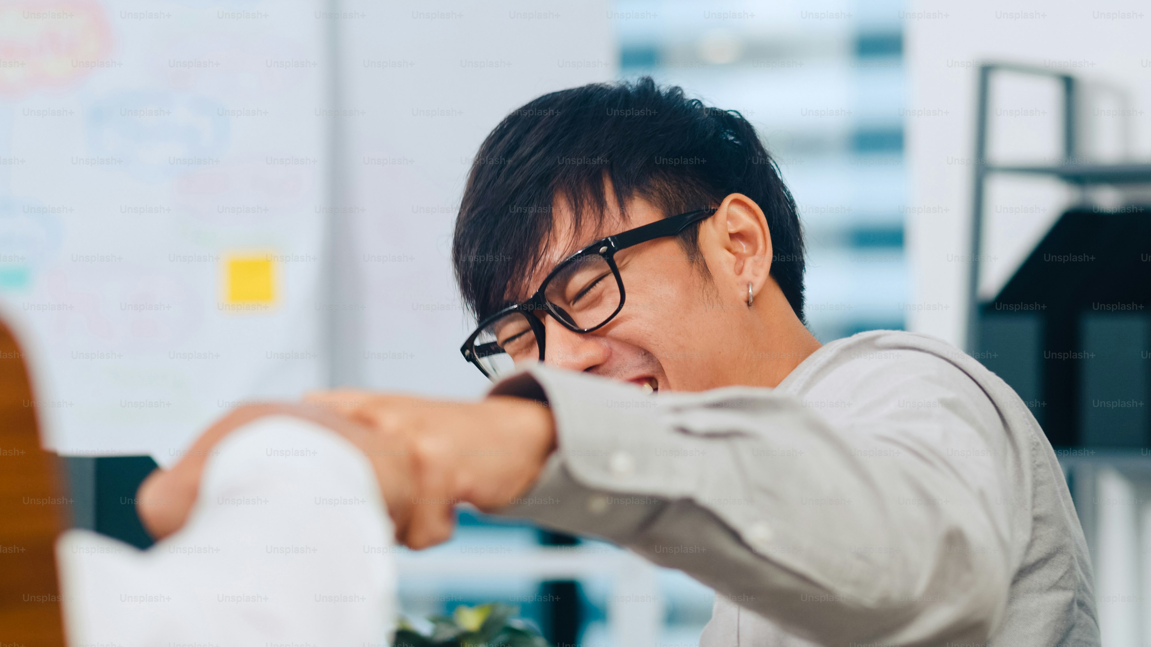 Seseorang berkacamata tertawa sambil memberi tinju di kantor