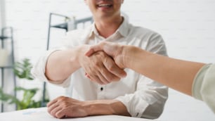 Multiracial group of young creative people in smart casual wear discussing business shaking hands together while sitting in modern office. Partner cooperation, coworker teamwork concept.