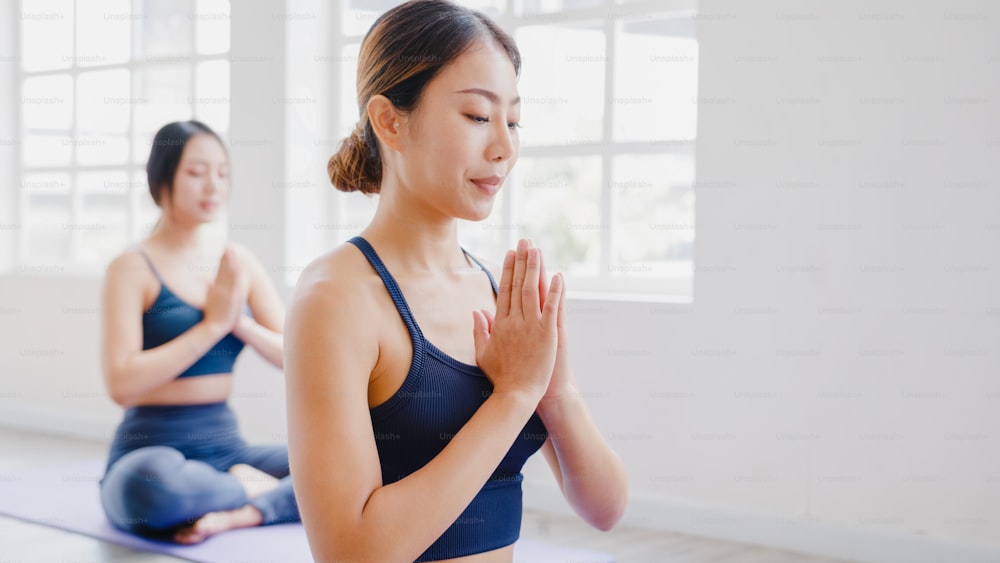 Young Asian sporty attractive people practicing yoga lesson with instructor. Asia group of women exercising healthy lifestyle in fitness studio. Sport activity, gymnastics or ballet dancing class.