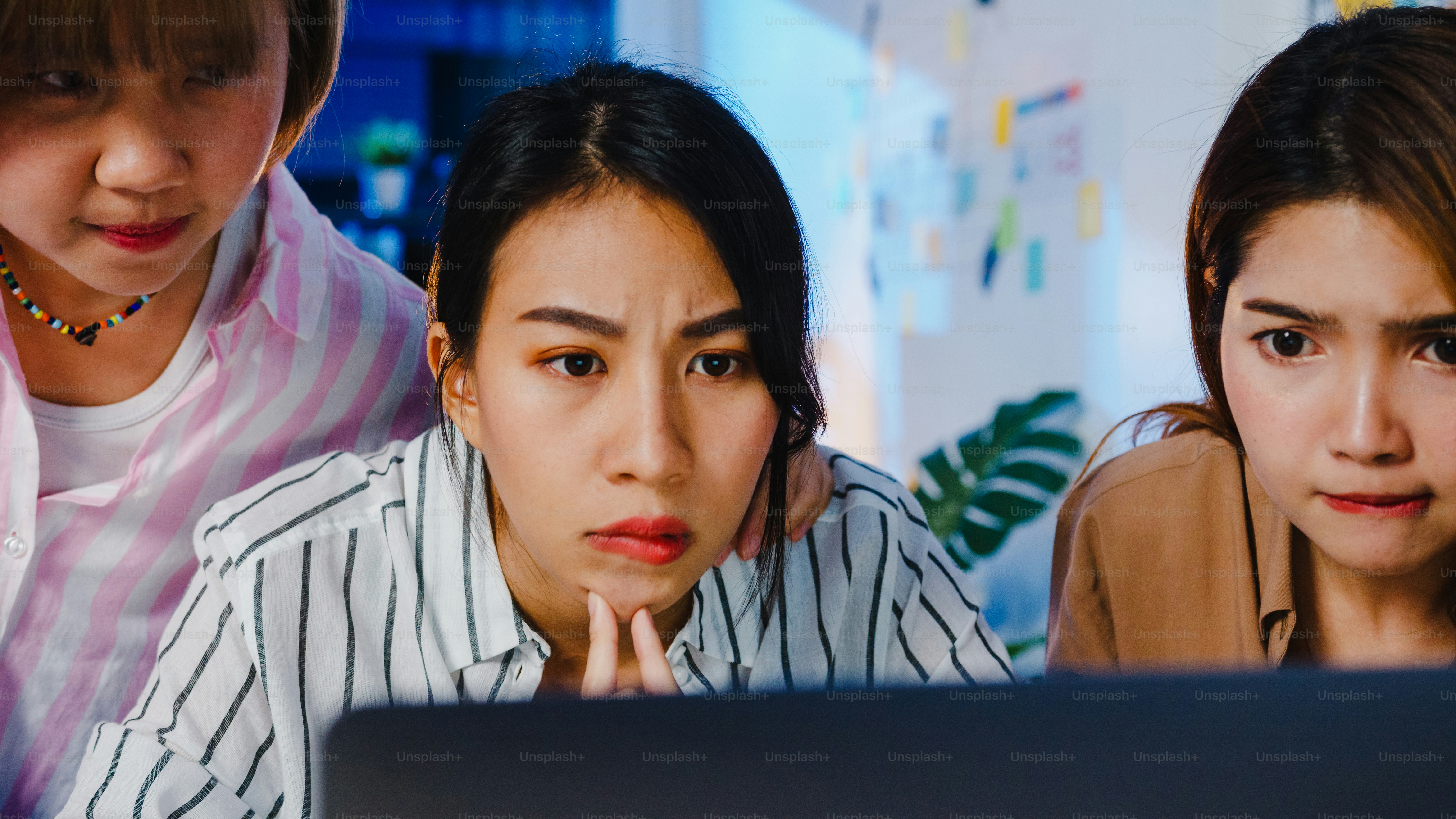 Three women looking at a laptop screen with focused expressions in an office