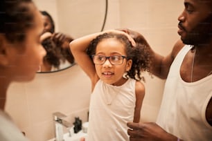 Bella ragazza bruna è seduta in bagno mentre suo padre le sta pettinando i capelli. Sta guardando sua sorella sognante e sorridente mentre chiacchiera con lei. Immagine