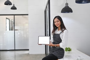 Friendly female business owner in apron showing digital tablet.