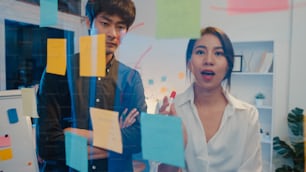 Empresários da Ásia ficam atrás de parede de vidro transparente ouvir gerente apontando o trabalho de progresso e reunião de brainstorm e trabalhador postar nota adesiva na parede. Inspiração de negócios, Compartilhe ideias de negócios.