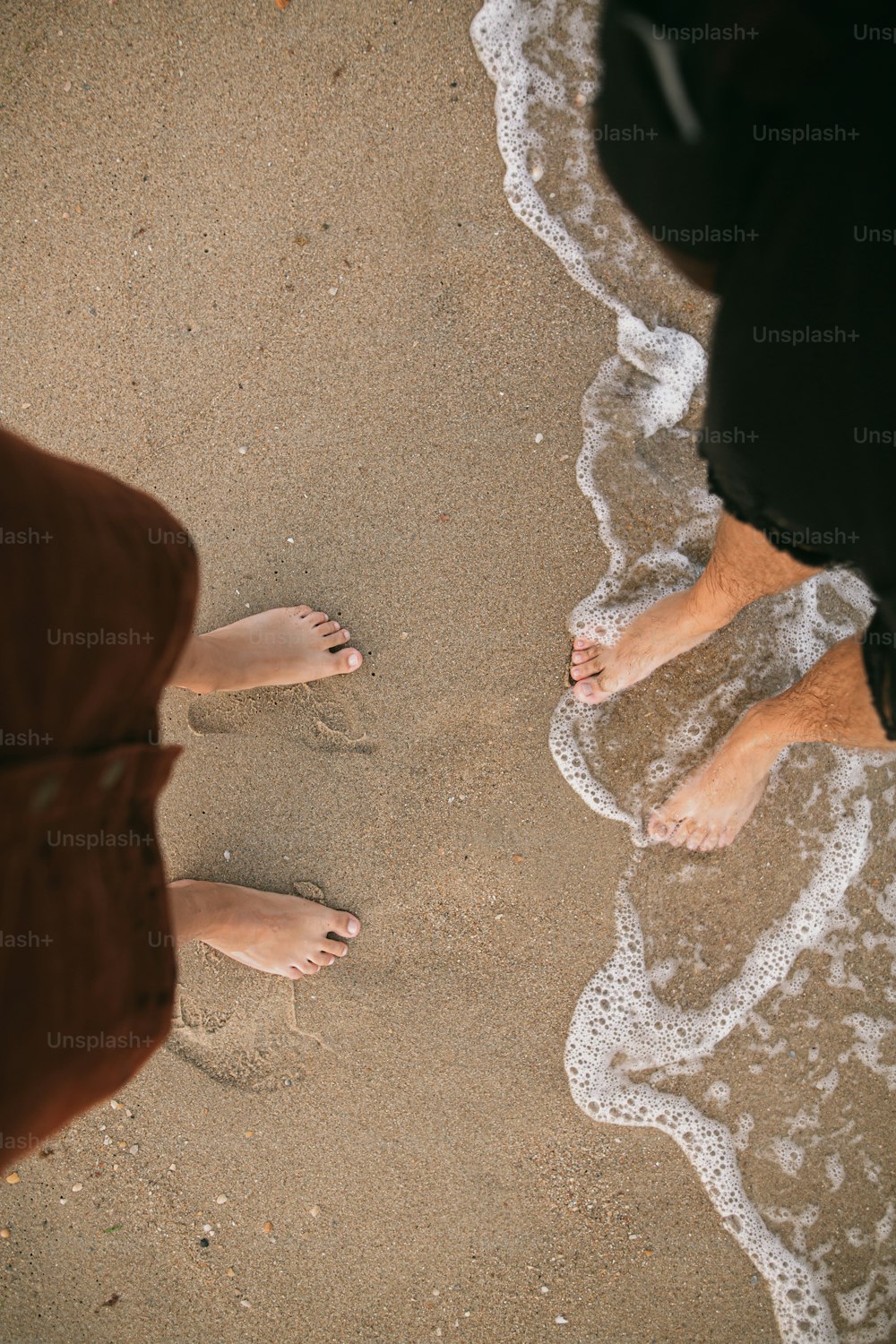 Carefree hipster couple standing walking barefoot on beach, top view. Feet in water foam, summer vacation. Tranquil moment. Mindfulness. Casual young family relaxing on seashore