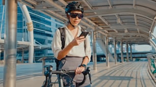 배낭을 메고 도시에서 스마트폰을 사용하는 행복한 아시아 사업가는 자전거를 타고 거리에 서서 사무실에서 일한다. 스포츠 소녀는 일을 위해 그녀의 전화를 사용합니다. 출퇴근, 시내 비즈니스 통근자.