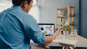 Young Asia businessman using laptop talk to colleagues about plan in video call meeting while work from home at living room. Self-isolation, social distancing, quarantine for corona virus prevention.