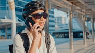 Mujer de negocios asiática con llamada de mochila llamada teléfono móvil hablar sonriendo en la calle de la ciudad ir a trabajar a la oficina. La chica deportista usa su teléfono para trabajar en negocios. Viaje al trabajo en bicicleta, viajero de negocios en la ciudad.
