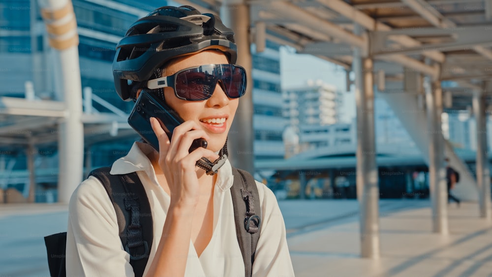 Asian businesswoman with backpack call mobilephone talk smiling in city street go to work at office. Sports girl use her phone for working business. Commute to work by bike, Business commuter in city.