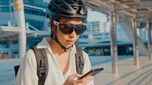 Femme d’affaires asiatique heureuse avec sac à dos utiliser un téléphone intelligent dans la ville se tenir dans la rue avec un vélo aller au travail au bureau. Une fille sportive utilise son téléphone pour travailler. Se rendre au travail, Trajet d’affaires en ville.
