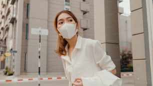 Successful young Asia businesswoman in fashion office clothes wear medical face mask walking alone outdoor in urban modern city in morning. COVID-19 outbreak pandemic, Business on the go concept.