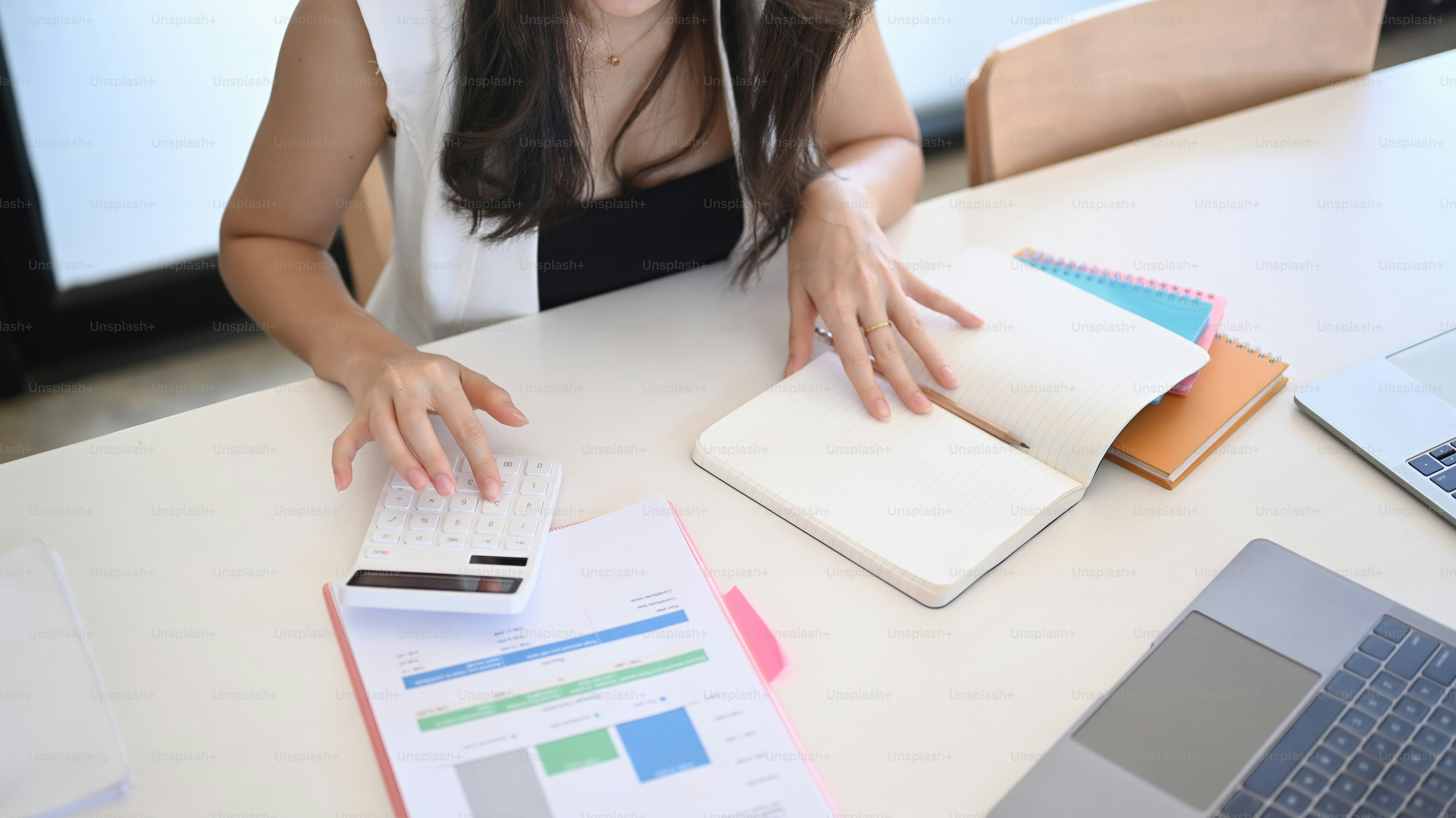 Cropped shot of accountant using calculator and reading information on notebook.