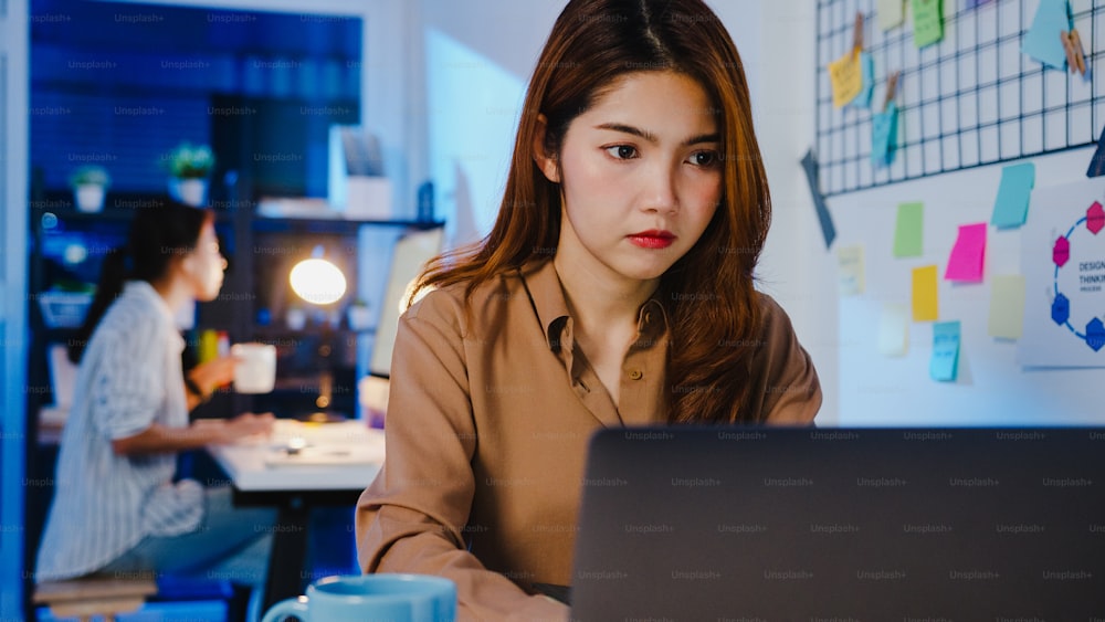 Happy Asia businesswoman social distancing in new normal situation for virus prevention while using laptop online business overtime back at work in office night. Life and work after coronavirus.