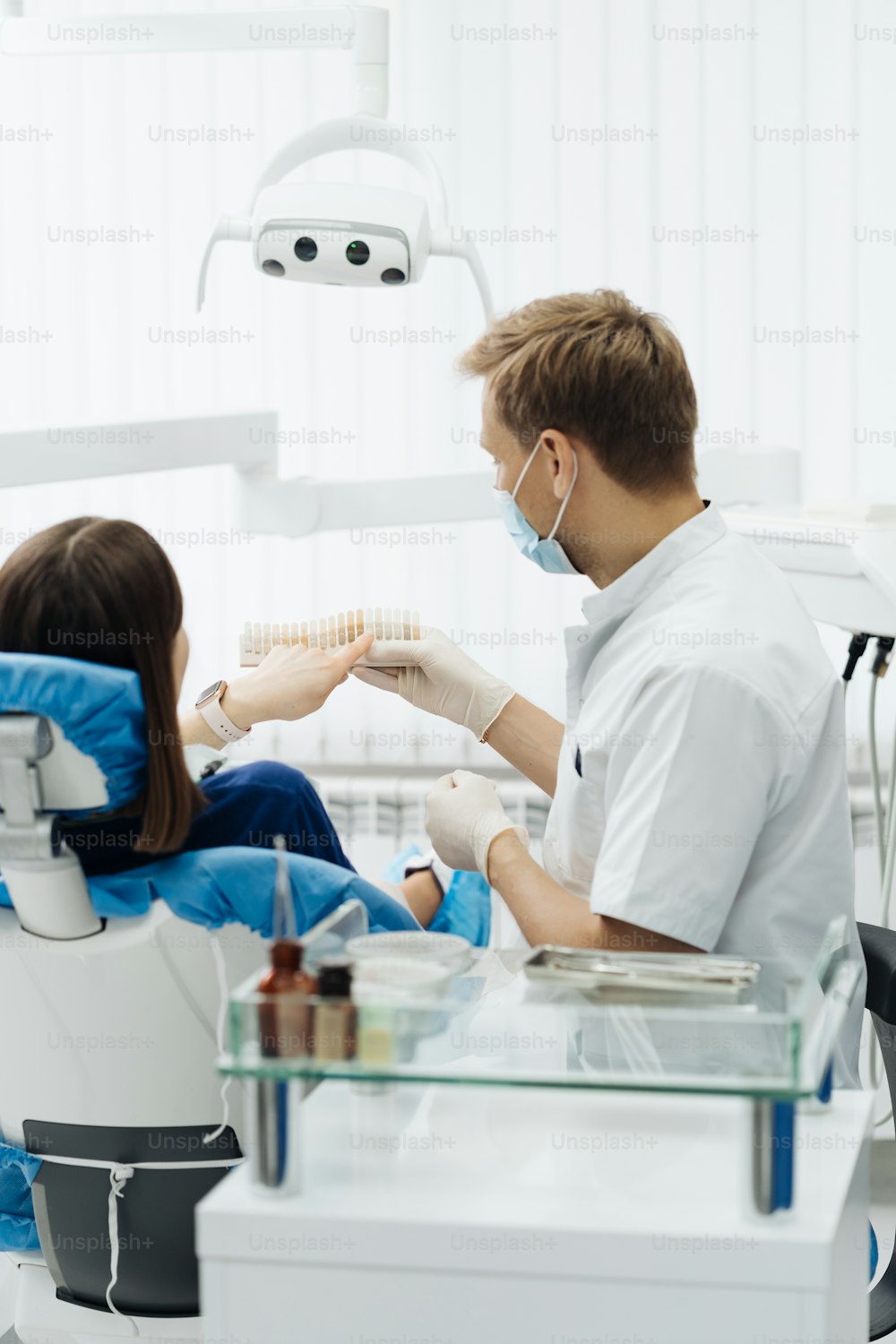 Young lady sitting in dental chair while stomatologist hands in sterile gloves holding tooth samples. She is smiling communicating and discussing with the dentist