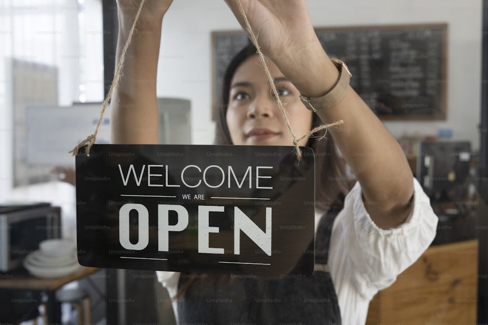 Female coffee shop owner  hanging the open sign on a glass door.