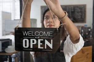 Female coffee shop owner  hanging the open sign on a glass door.