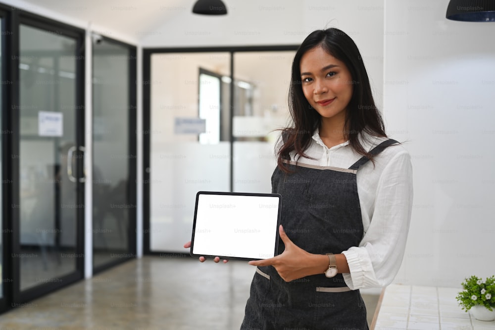 Asian woman waitress holding and showing digital tablet while standing in coffee shop.