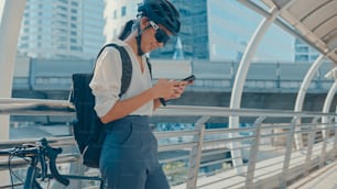 Femme d’affaires asiatique heureuse avec sac à dos utiliser un téléphone intelligent dans la ville se tenir dans la rue avec un vélo aller au travail au bureau. Une fille sportive utilise son téléphone pour travailler. Se rendre au travail, Trajet d’affaires en ville.