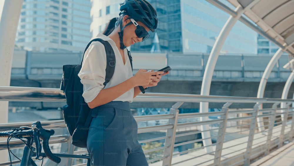Happy asian businesswoman with backpack use smart phone in city stand at street with bike go to work at office. Sport girl use her phone for working job. Commute to work, Business commuter in city.
