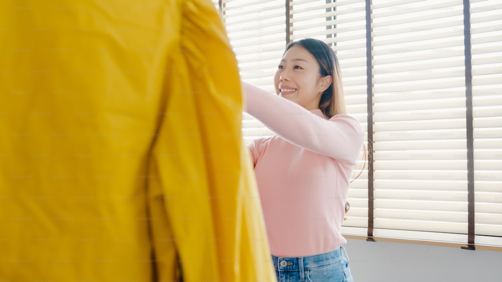 Beautiful attractive young Asia lady choosing her fashion outfit clothes in closet at house or store. Girl think what to wear casual shirt. Home wardrobe or clothing shop changing room.