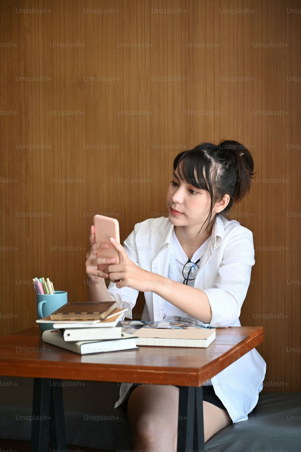 Retrato de una mujer joven con ropa informal sentada en un café y usando un teléfono móvil.