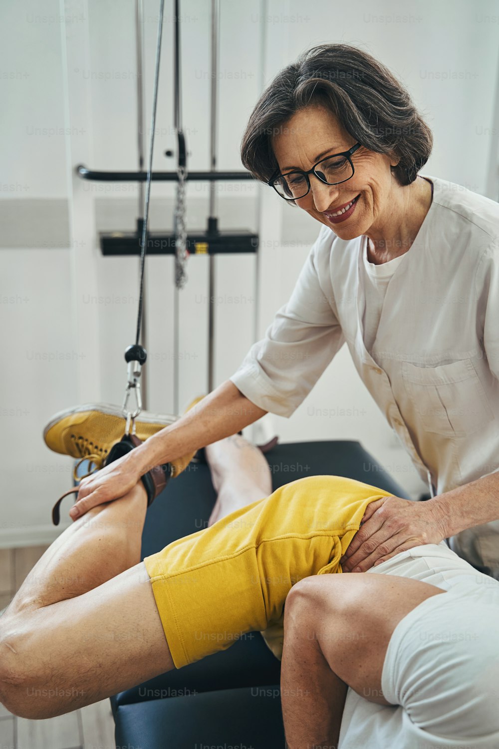 Smiling professional physiatrist assisting a man with the side-lying leg lift during the physiotherapy session