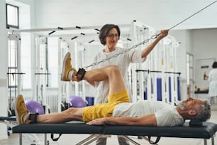 Side view of a gray-haired male athlete doing the knee flexion on the gym equipment