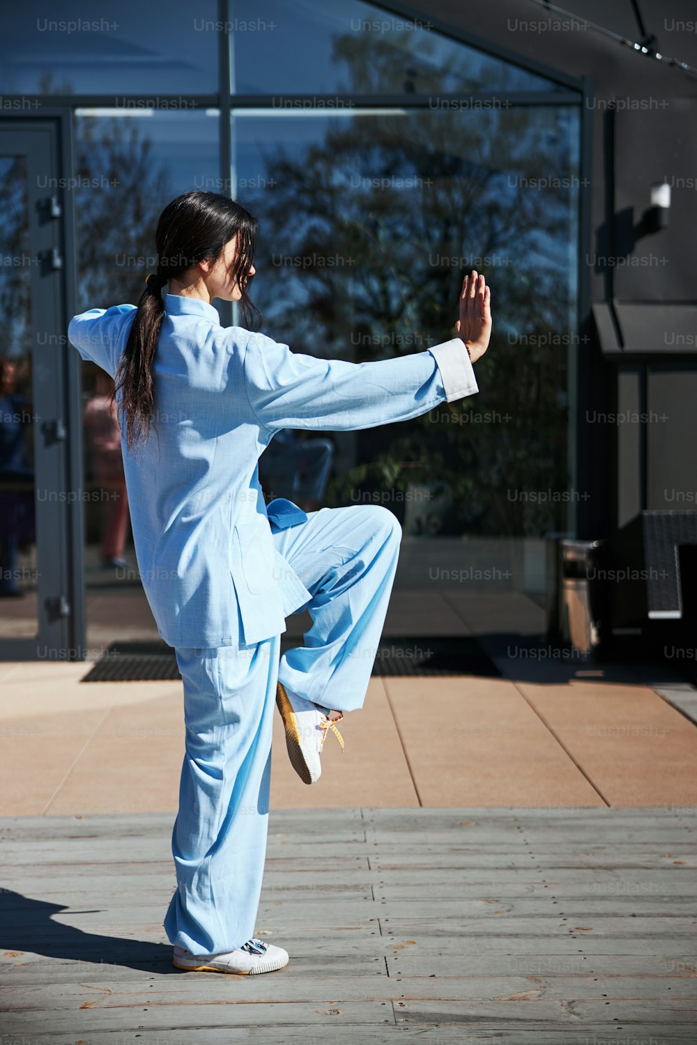 Konzentrierte Frau im chinesischen Anzug, die auf einem Fuß steht und beim Training die Hand nach vorne legt