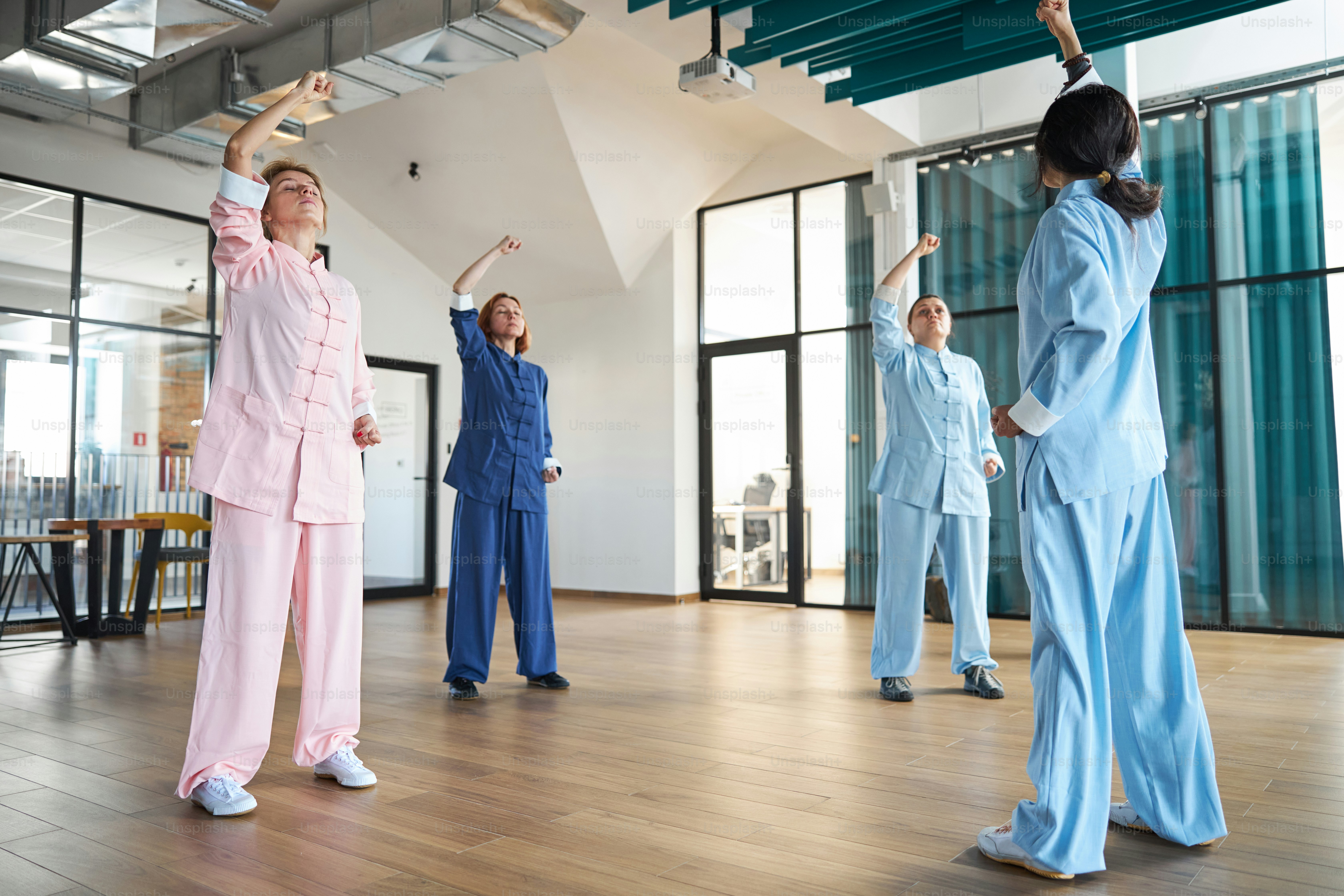 Quattro donne in abiti cinesi che alzano i pugni e provano la respirazione ritmica profonda durante la lezione di qigong