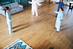 Mujeres jóvenes de pie frente a la maestra de qigong y repitiendo los movimientos después de ella en una habitación espaciosa