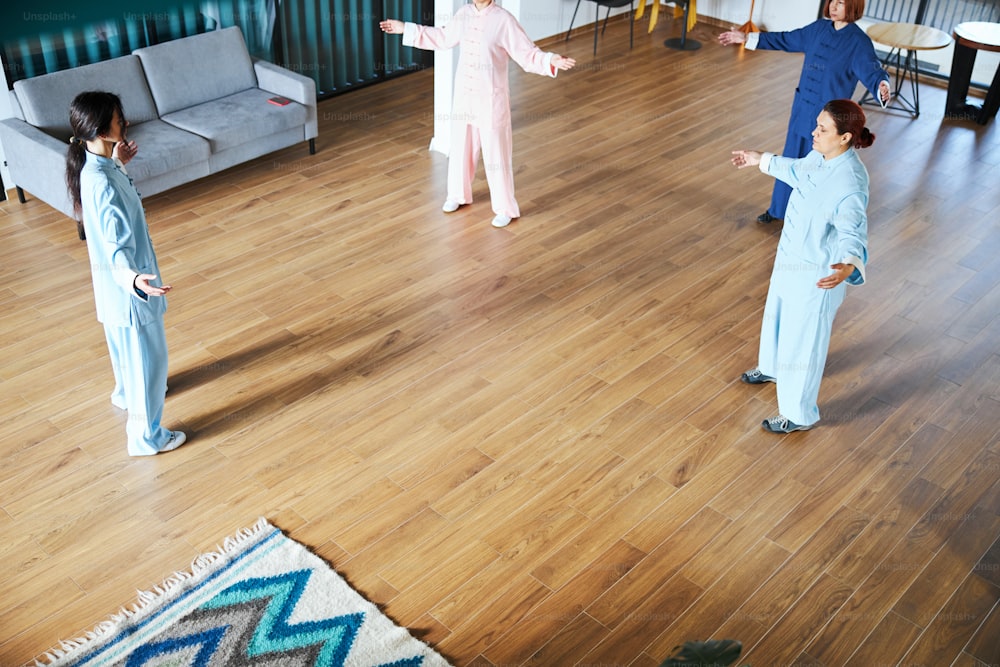 Young women standing in front of the qigong master and repeating the movements after her in a spacious room