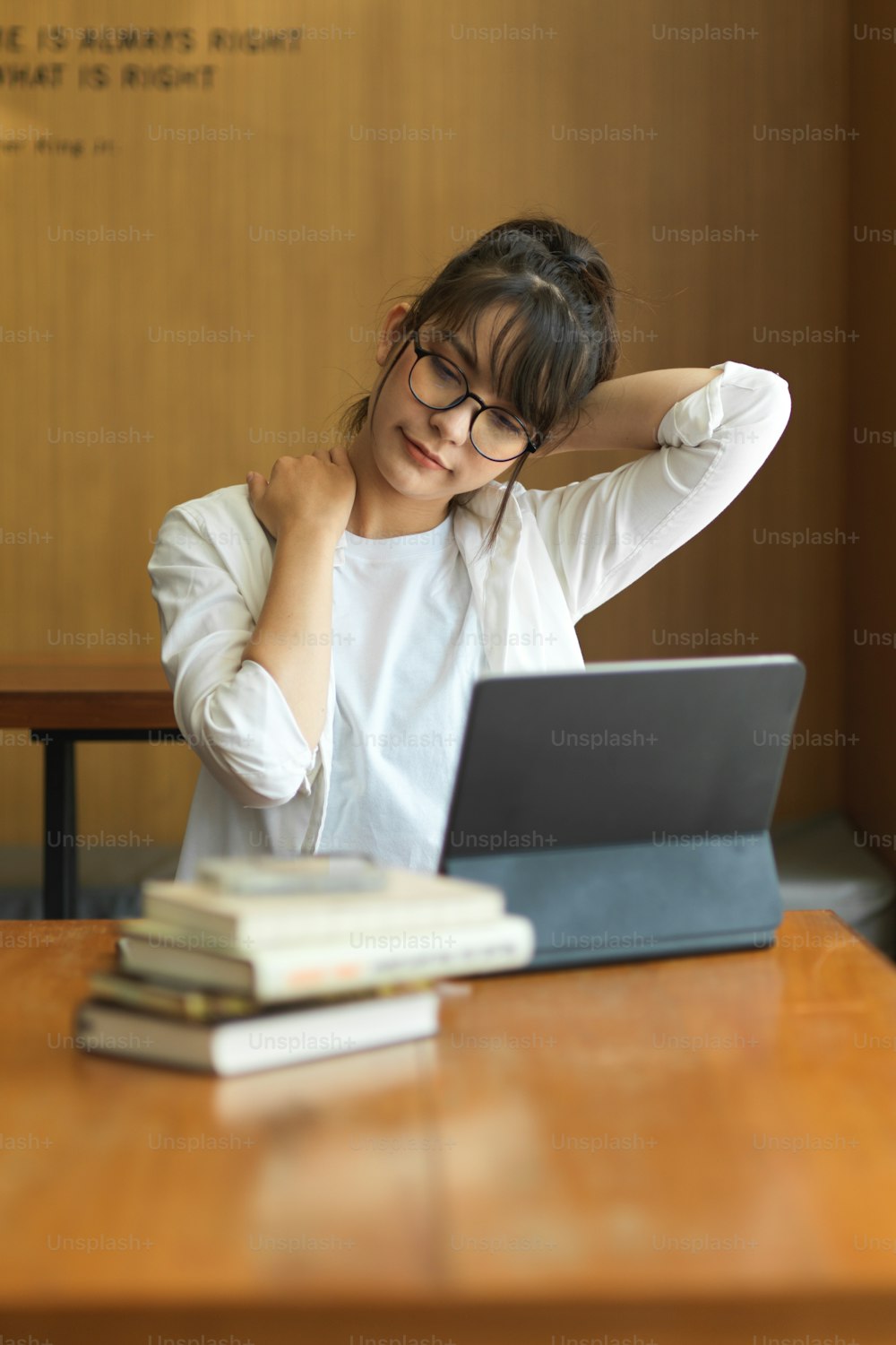 Portrait of female student relaxing and stretching her neck while preparing for exam in library