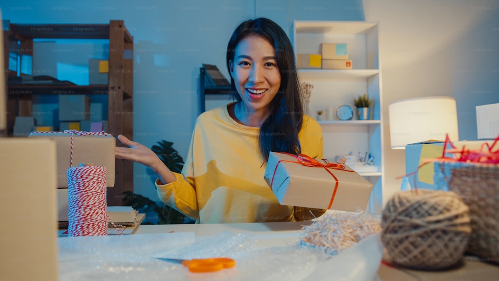 Happy young Asia businesswoman looking at camera selling introduce product to client video live streaming in online shop marketplace at night. Small business owner, online market delivery concept.