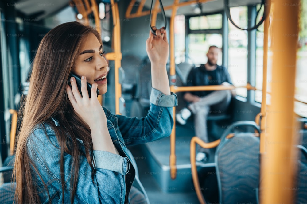 Young beautiful passengers in a moving bus using smartphones and talking during a ride