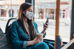 Donna che indossa una maschera protettiva mentre guida un autobus e si siede a distanza dagli altri passeggeri a causa della pandemia di covid19