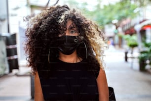 コロナウイルスに対するサージカルマスクを着用して街の通りを歩くアフロウーマン。パンデミック時の社会的距離を尊重するフェイスマスクの女の子。