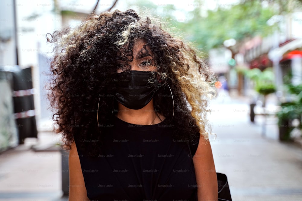 Afro-Frau geht auf der Straße der Stadt mit chirurgischer Maske gegen die Krankheit Coronavirus. Mädchen mit Gesichtsmaske, das die soziale Distanzierung während der Pandemie respektiert.
