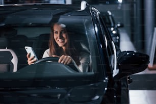 La mujer joven está dentro de un nuevo automóvil moderno con teléfono.