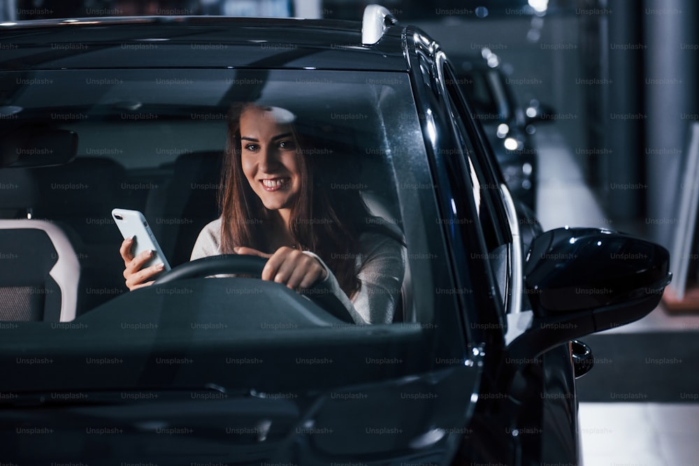 La giovane donna è all'interno di un'automobile moderna nuova di zecca con il telefono.