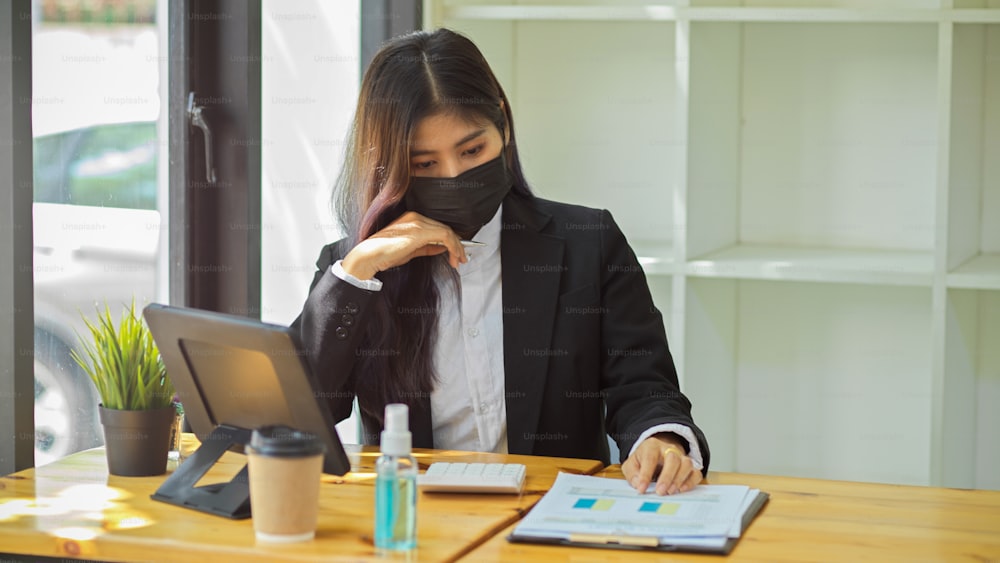 Half-length portrait of businesspeople with face mask working with digital tablet and paperwork in office