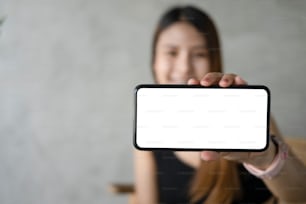 Smiling beautiful woman holding and showing mock up mobile phon with empty screen.