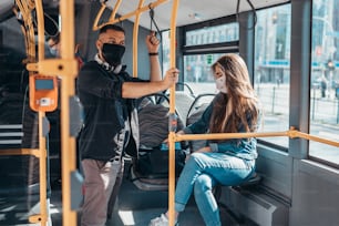 Jeunes passagers dans le bus portant un masque de protection et se tenant à distance en raison de la pandémie de coronavirus