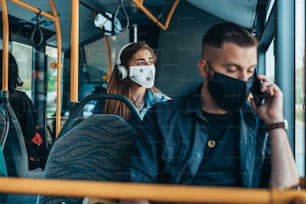 Jovens passageiros no ônibus usando máscara de proteção e usando smartphone enquanto se sentam à distância devido à pandemia de coronavírus