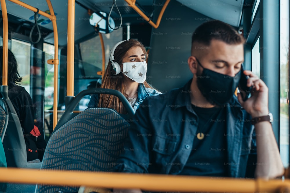 Young passengers in the bus wearing protective mask and using smartphone while siting on a distance due to corona virus pandemic