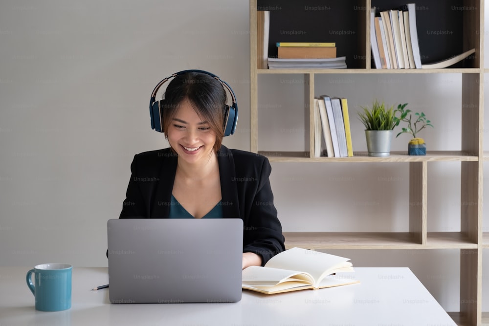 Una mujer alegre con auriculares se concentra en un seminario web en su computadora portátil