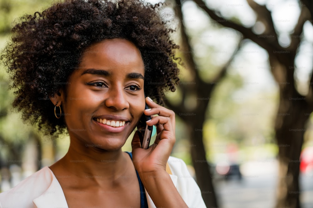 Retrato de una mujer de negocios afro hablando por teléfono mientras está de pie al aire libre en el parque. Concepto de negocio.