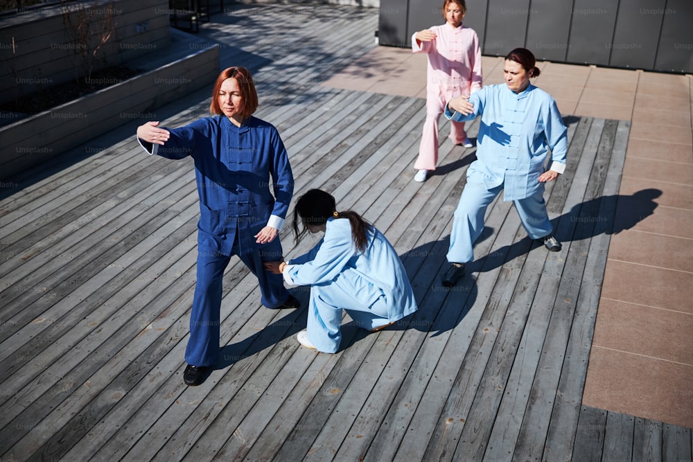 Several women practicing Chinese martial arts and their teacher carefully correcting their legs position