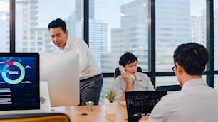 Millennial group of young Asia businesspeople in small modern office. Japanese male boss supervisor teaching intern or new employee Chinese young guy helping with difficult assignment at meeting room.