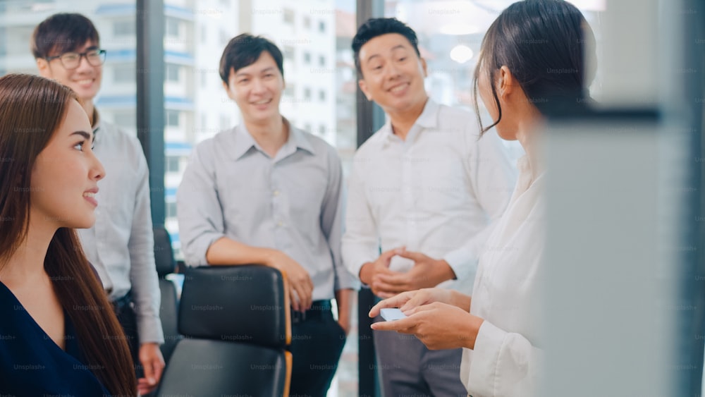 Uomini e donne d'affari asiatici che si incontrano, brainstorming di idee, conduzione di progetti di presentazione aziendale, colleghi che lavorano insieme, pianificano la strategia di successo, godono del lavoro di squadra in un piccolo ufficio moderno.