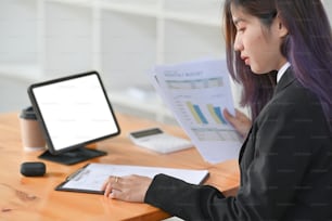 コンピュータテーブルの前に座り、現代のオフィスで財務データを分析しているビジネスウーマンの側面図。