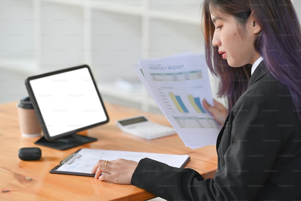 Seitenansicht einer Geschäftsfrau, die vor einem Computertisch sitzt und Finanzdaten in einem modernen Büro analysiert.